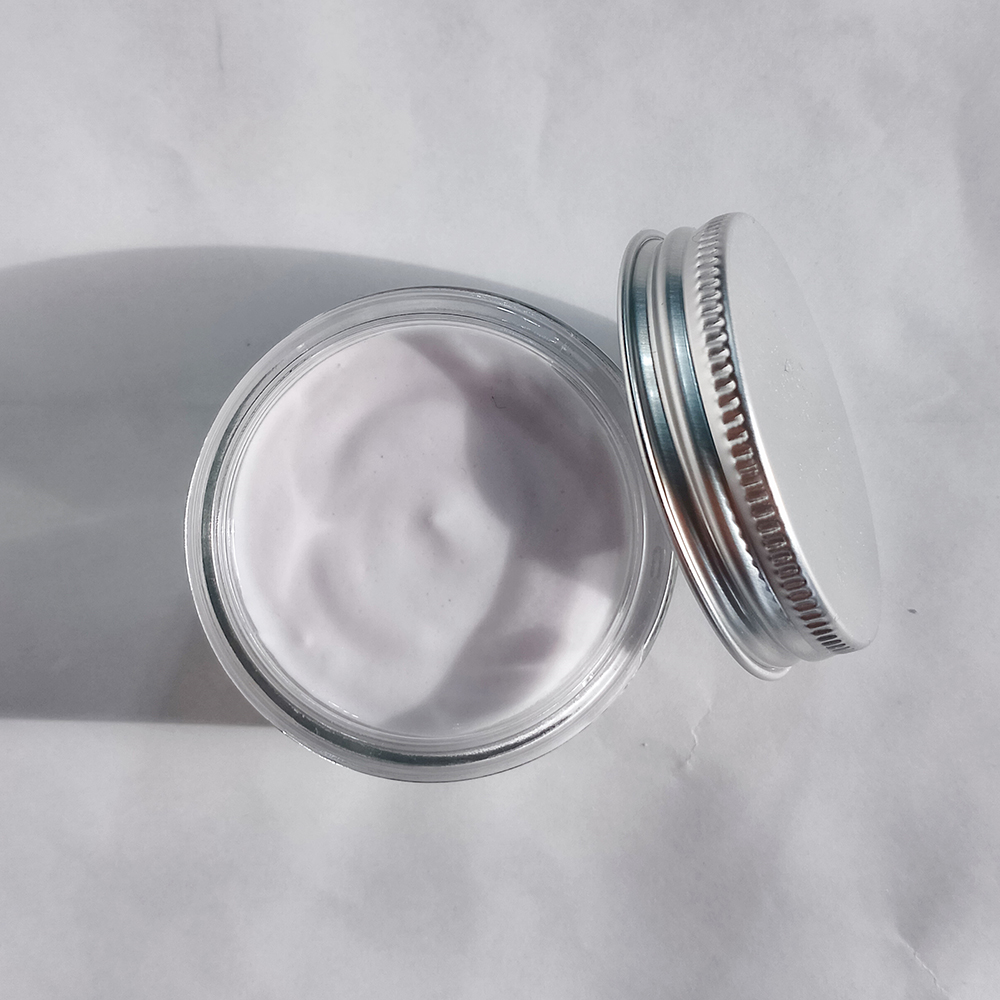 Hydratačný pleťový jogurt bielej farby v sklenenej nádobe s kovovým viečkom na bielom pozadí.